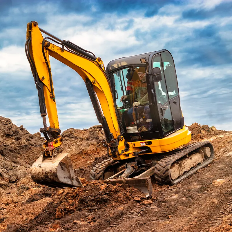 Minibagger auf der Baustelle am Rand einer Grube vor bewölktem blauem Himmel